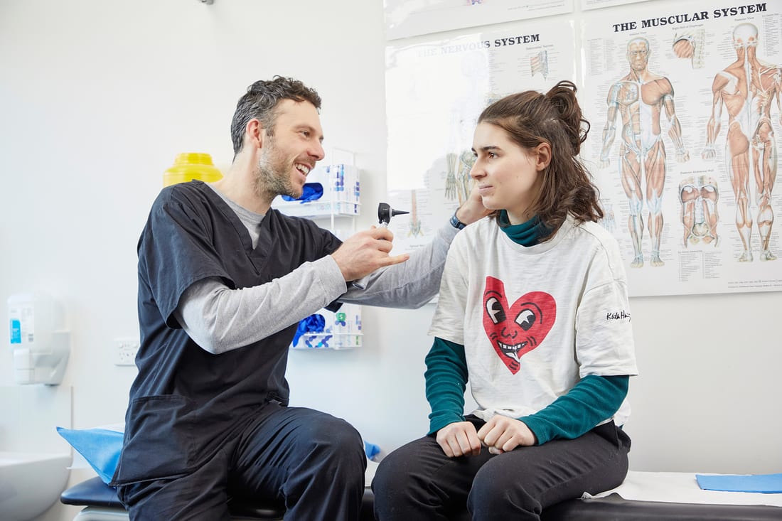 Dr Dan Epstein smiling while checking a patient's ear with an otoscope